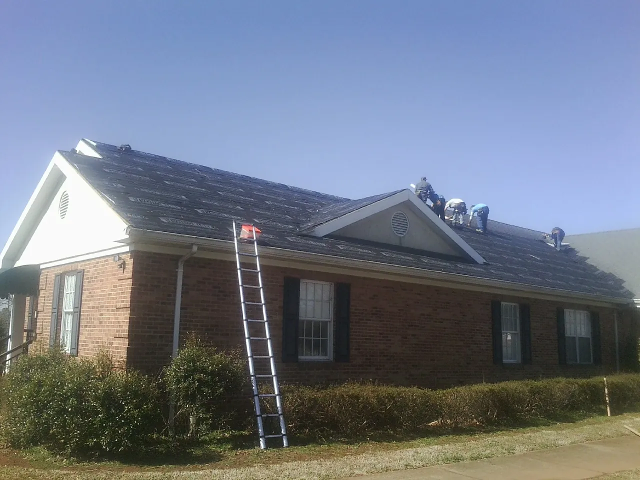 Crew tearing shingles off a brick ranch roof with a ladder set — Emergency Roof Repair work by our crew in Augusta